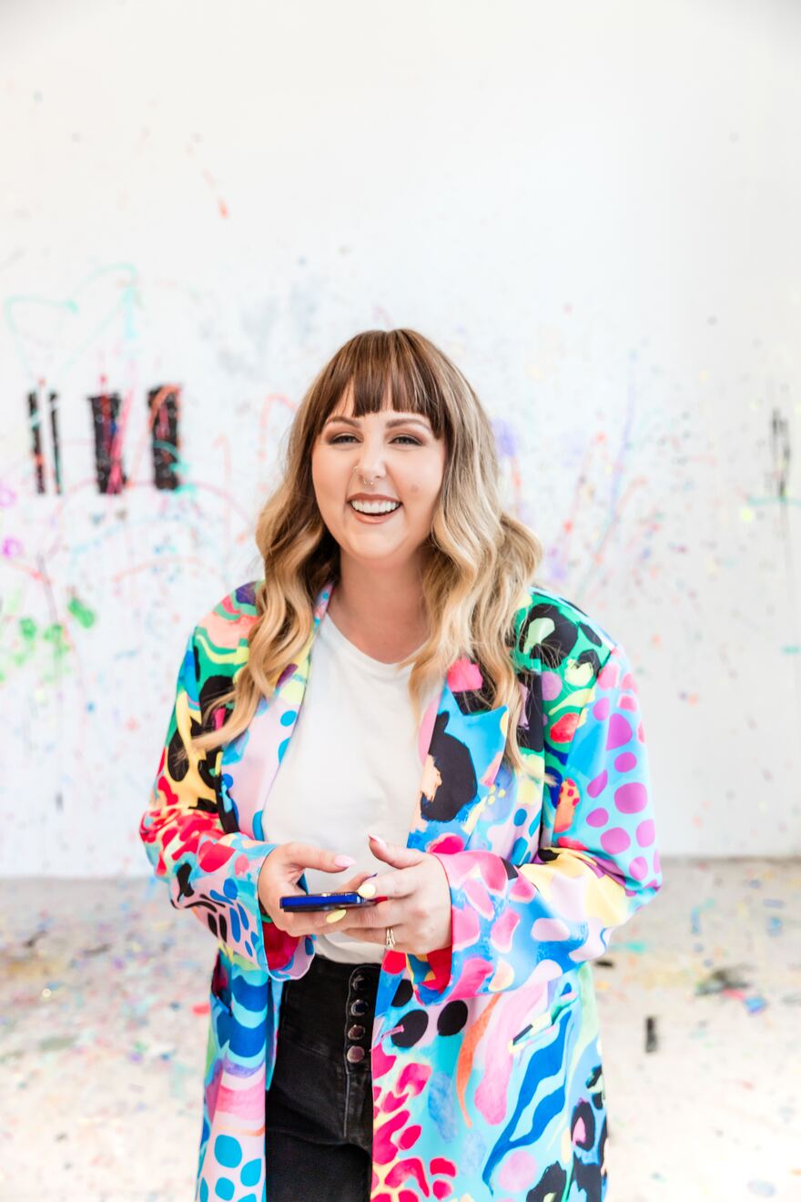 Kayla, founder of That Socials Team, in a colorful paint-splattered jacket